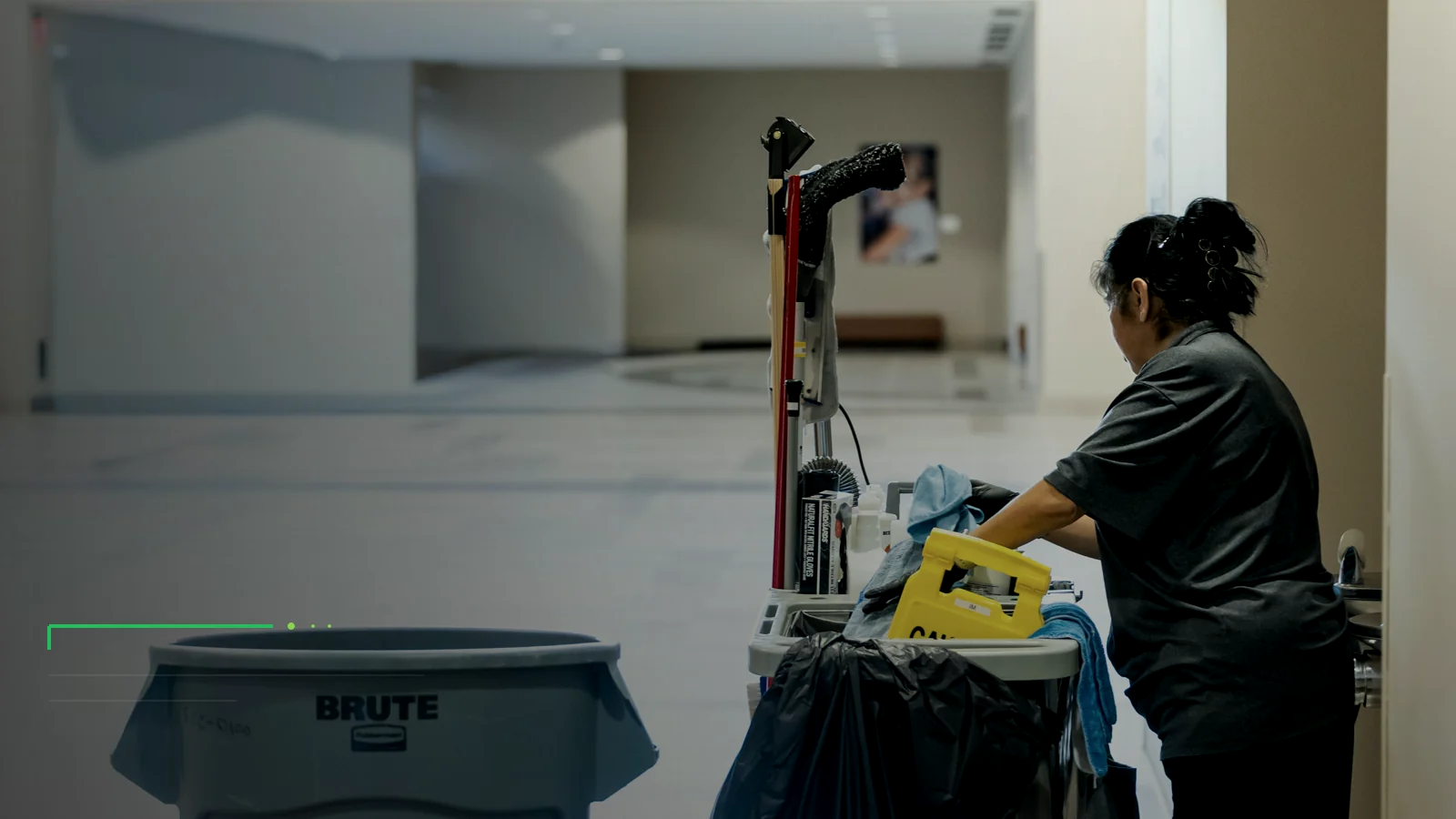 Illustrative custodial professional preparing equipment in a school corridor.